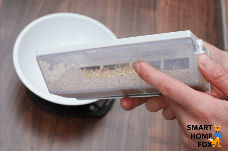 Staubbehälter mit den aufgesaugten Haferflocken wird in die Kamera gehalten